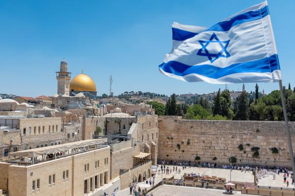 An Israeli flag blows in the wind from an elevated view of the Western Wall. Jewish orthodox believers read the Torah and pray facing the Western Wall, also known as Wailing Wall or Kotel in Old City in Jerusalem, Israel. It is small segment of the structure which originally composed the western retaining wall of the Second Jewish Temple atop the hill known as the Temple Mount to Jews and Christians.